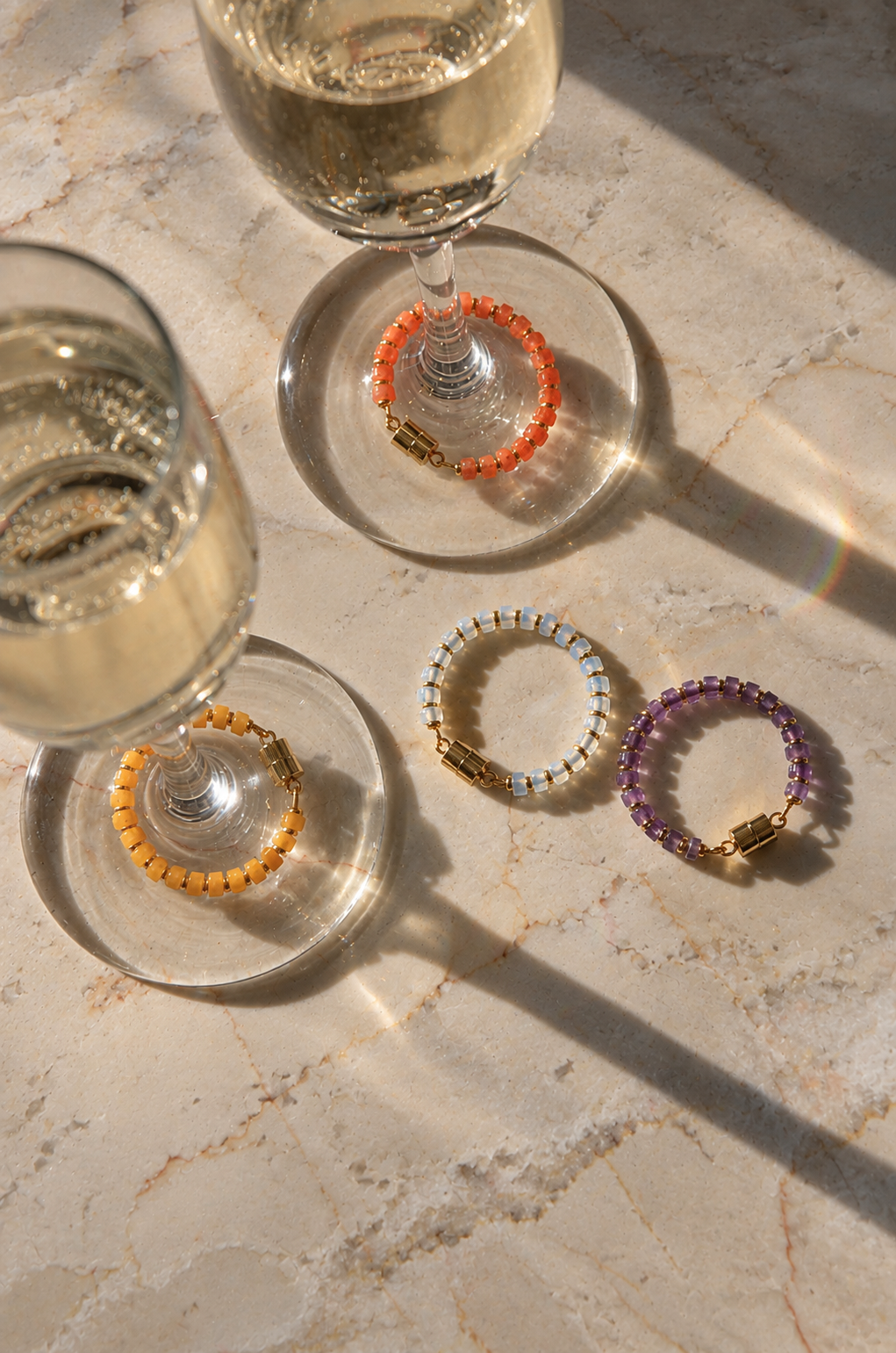 Spellbound magnetic wine charms in Opal, Amethyst, Citrine and Mandarin Garnet with gold hardware on sparkling wine glasses in afternoon sun